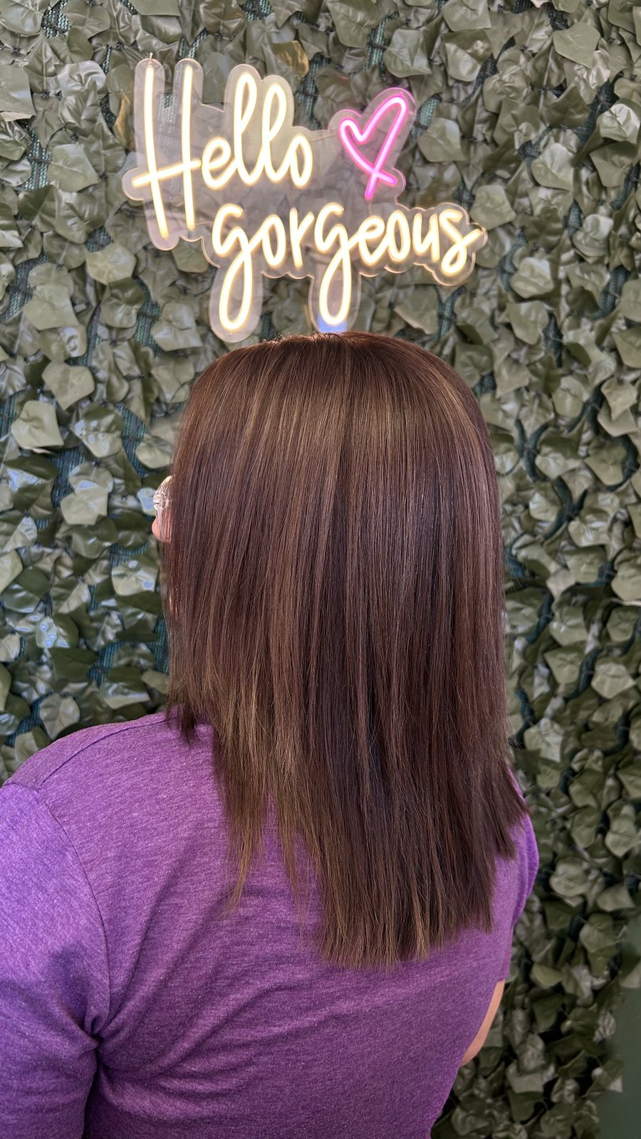 Sleek cherry-toned lob in front of the 'hello gorgeous' neon.